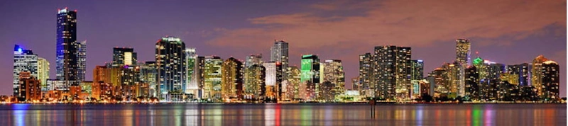 Miami skyline at dusk with illuminated buildings reflected on the water promoting Limo Service Miami